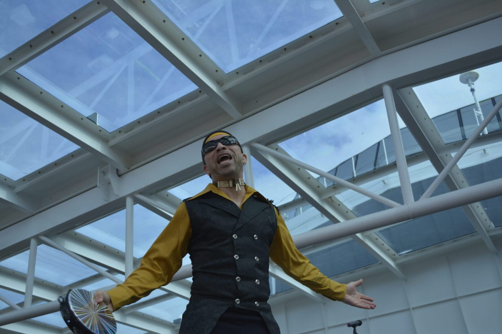 A man in a yellow shirt and black vest standing under a glass ceiling.