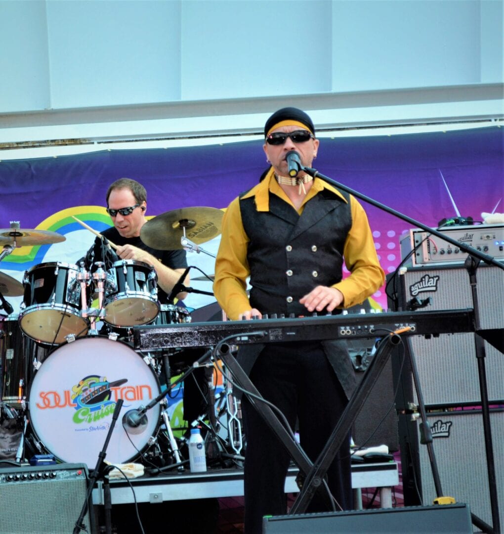 A man in sunglasses and a yellow shirt playing keyboard.
