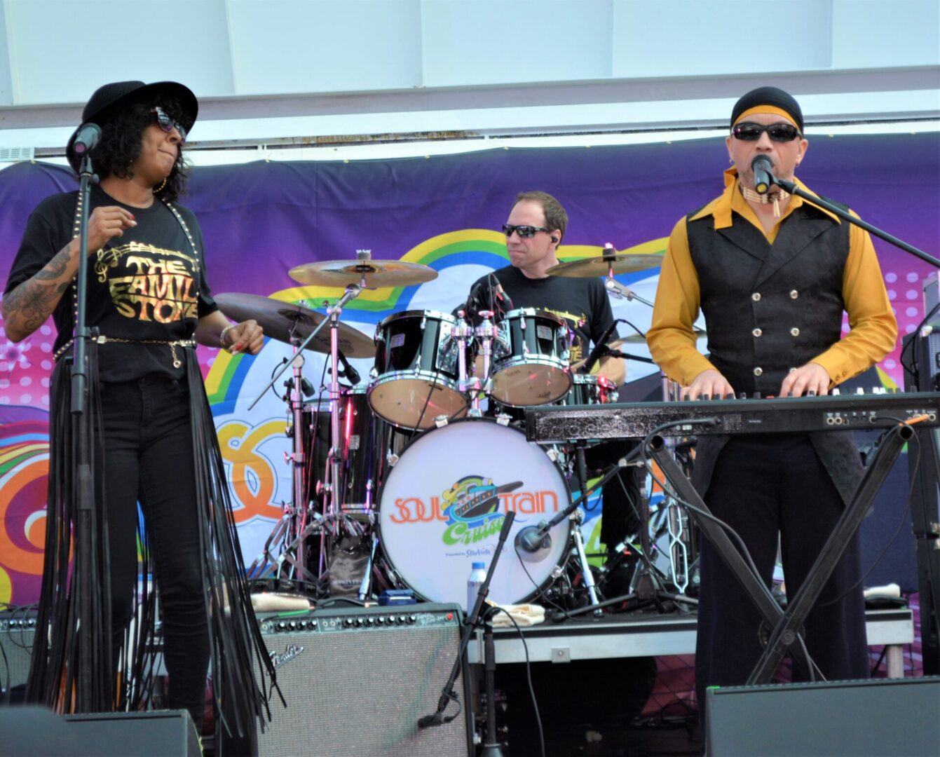 A band performing on stage with a rainbow background.