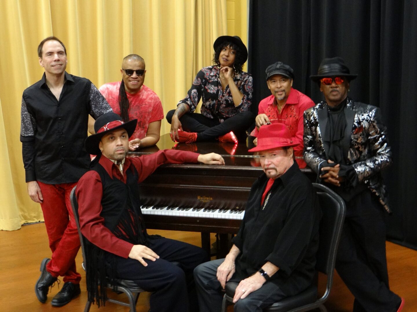 The Family Stone band in red outfits posing near a piano