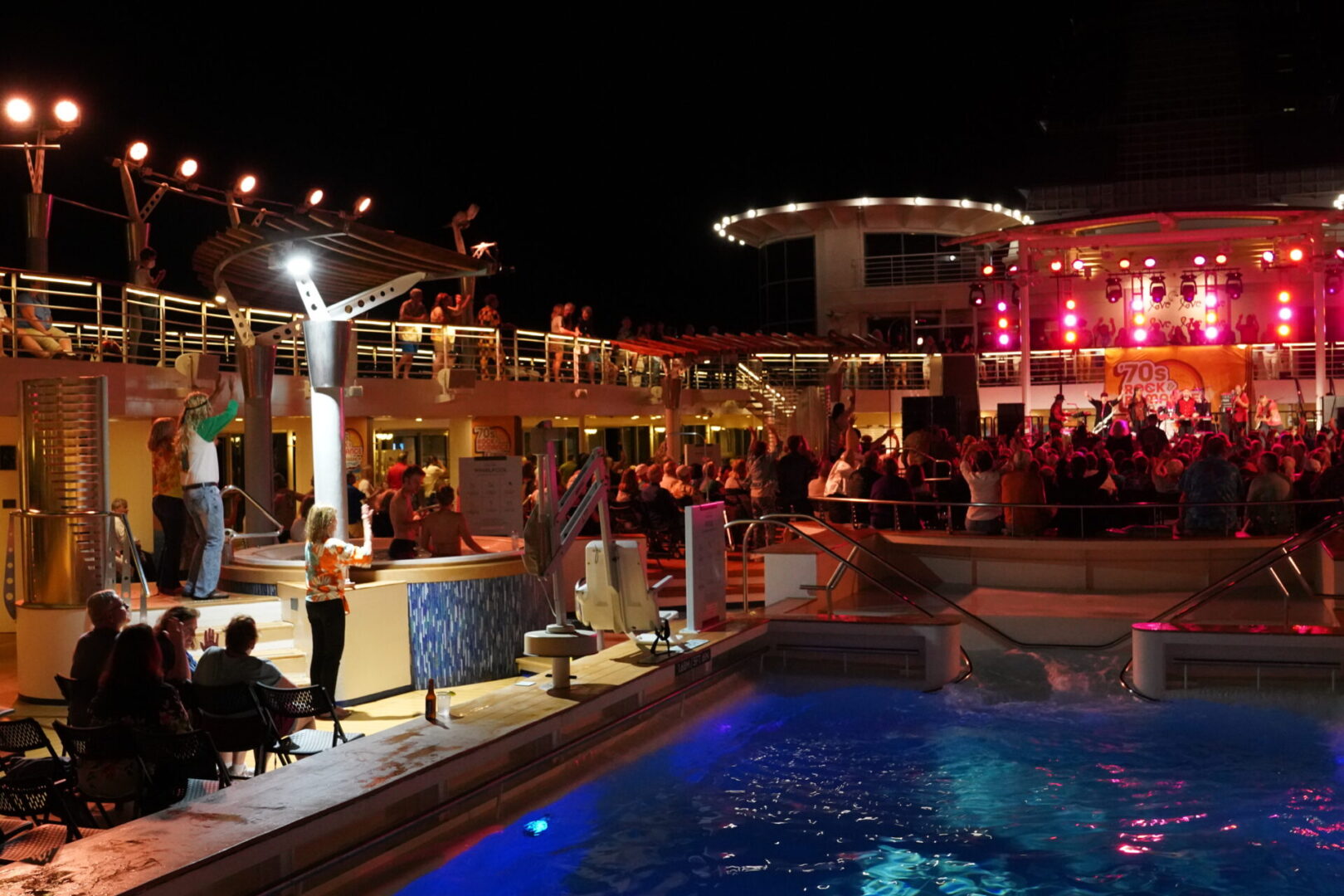 A pool with people sitting at it and a bar in the background.