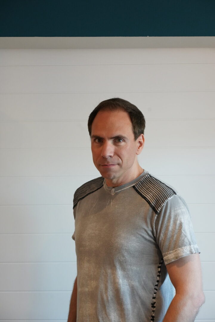 A man in grey shirt standing next to wall.